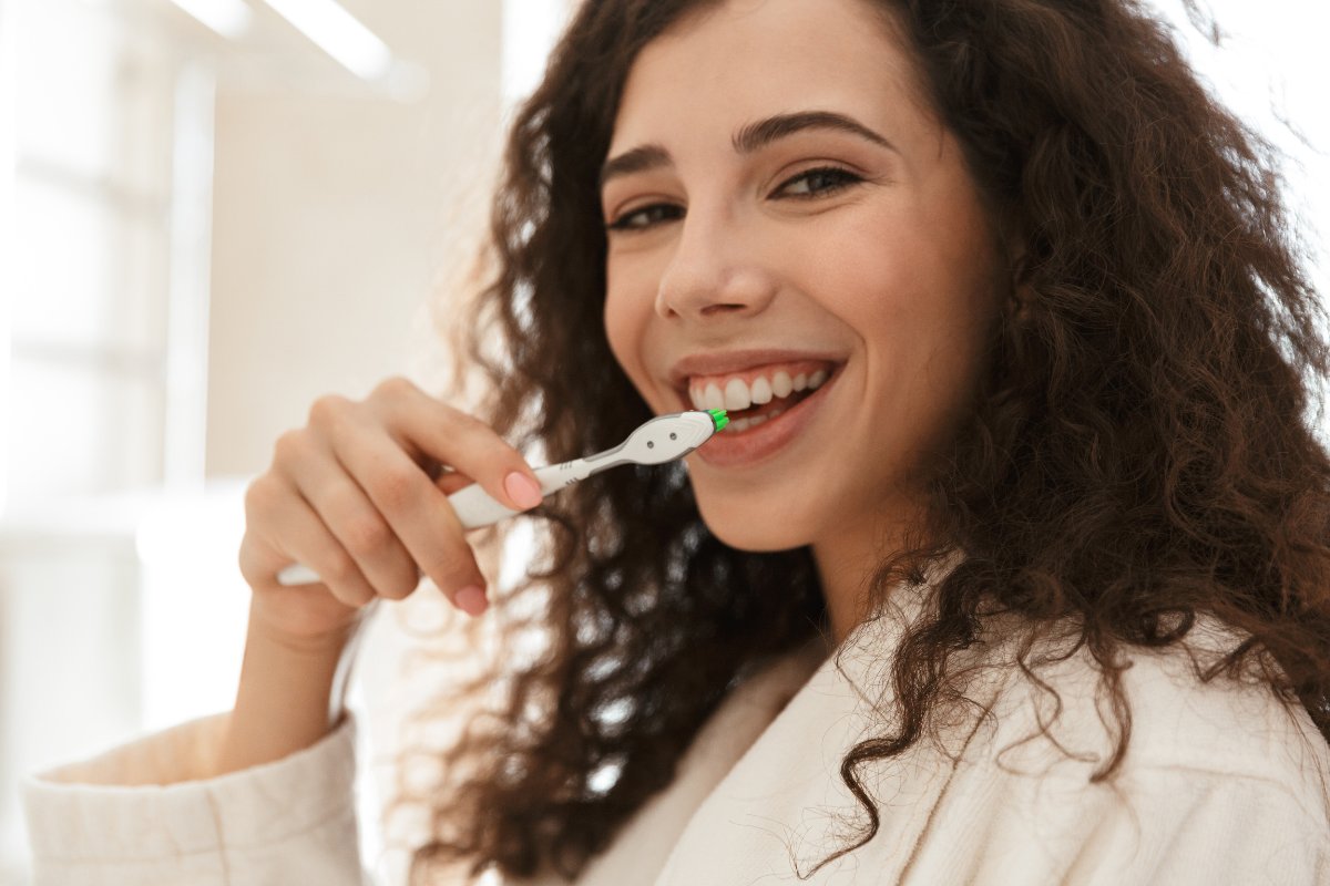 Woman smiling while brushing teeth in bright bathroom setting at dental center