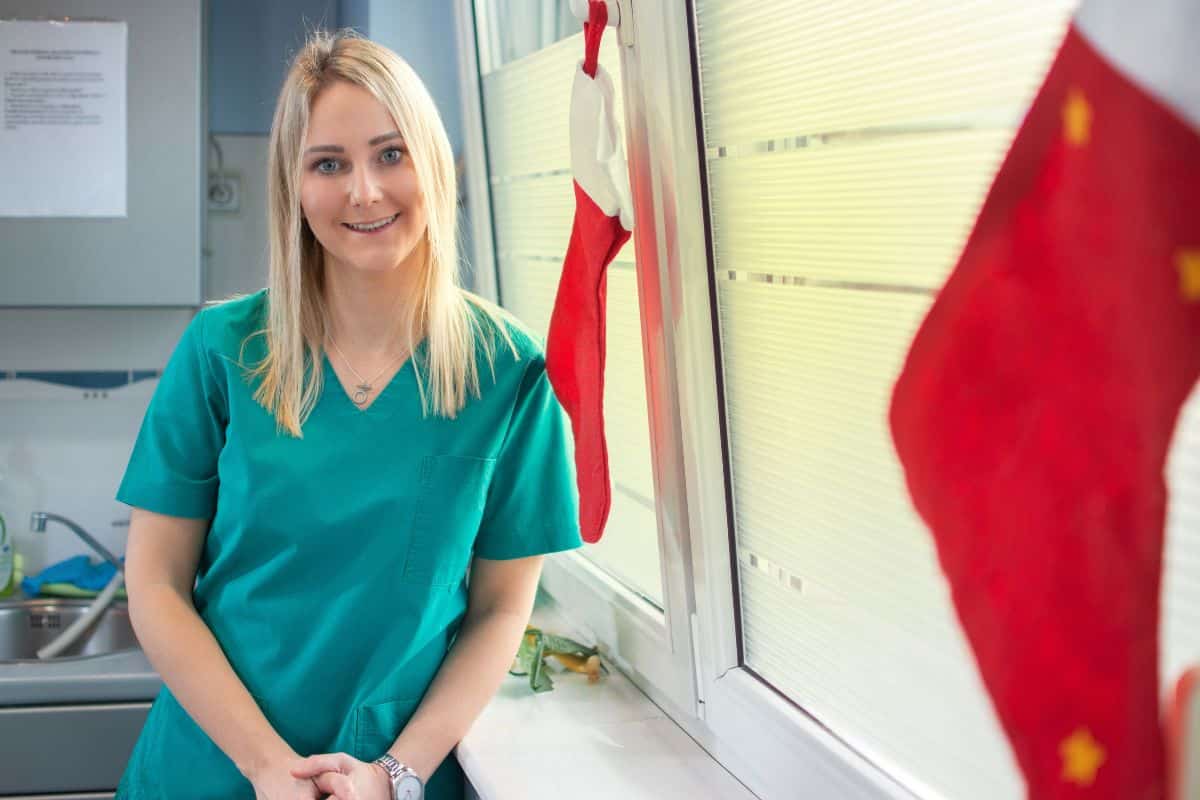 Female dental professional in teal scrubs smiling in modern dental office setting.